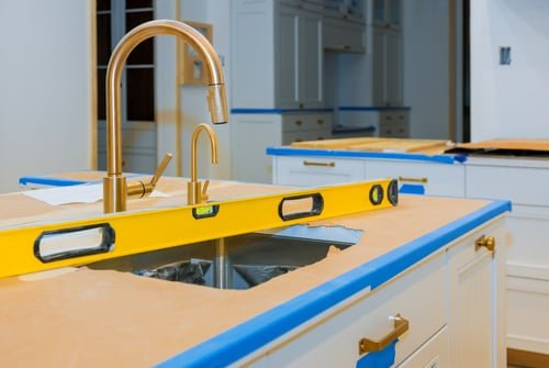 Kitchen counter mid-installation with a brass faucet and taped undermount sink cutout