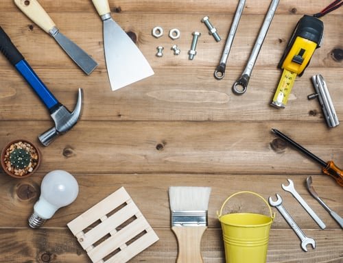 Hand tools, a paint brush and a tape measure laid out on a workbench